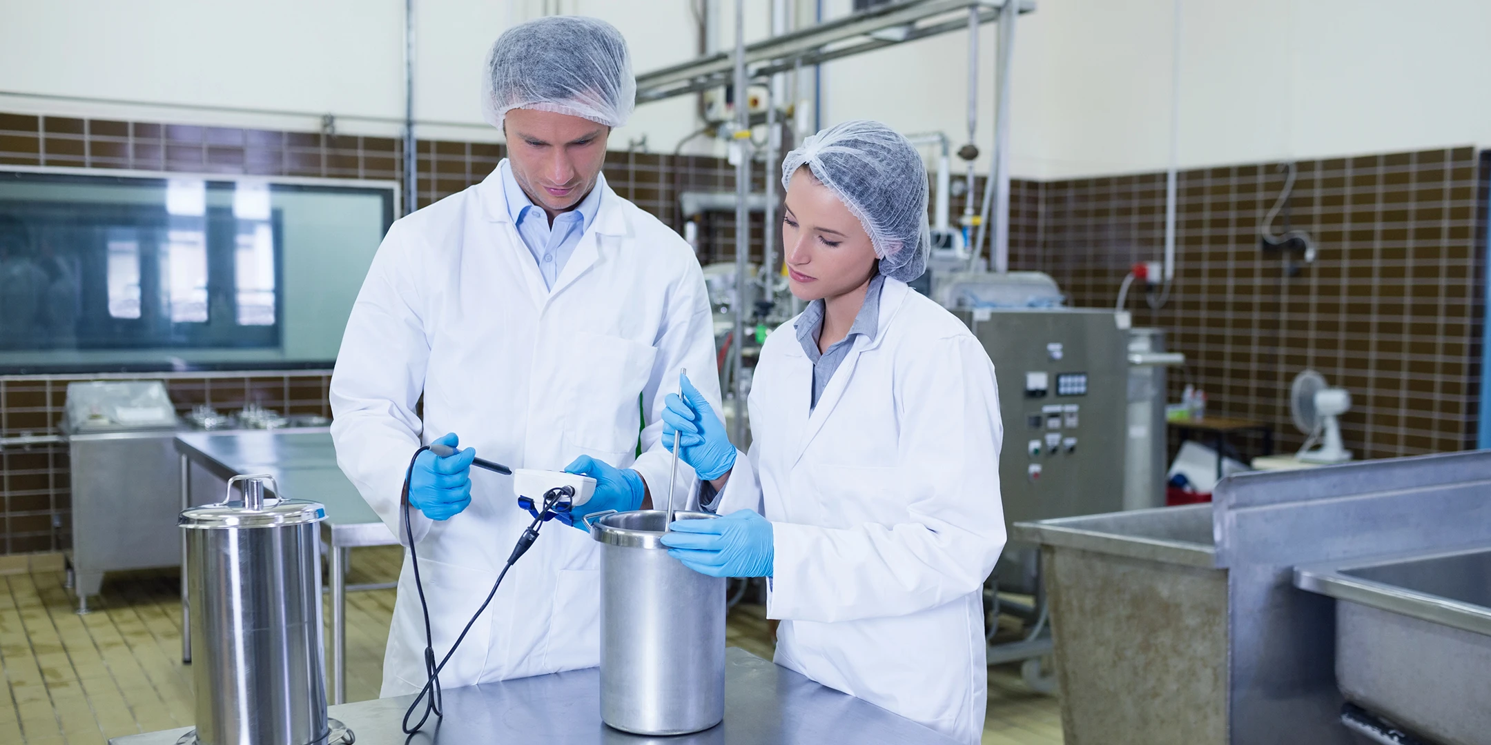 Two employees in protective clothing examine a food sample according to HACCP